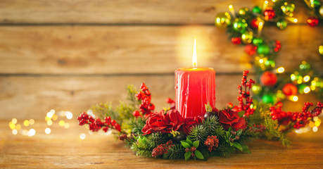 Burning Christmas red candle and  festive Christmas arrangement on a wooden table.