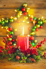 Burning Christmas red candle and  festive Christmas arrangement on a wooden table.