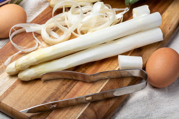 Bunch of fresh uncooked white asparagus and peeler knife, how to peel asparagus vegetables