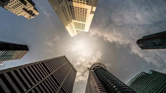 Time lapse - Looking up to business and financial skyscraper buildings in Singapore with  moving clouds and sun in the sky at Singapore central financial district