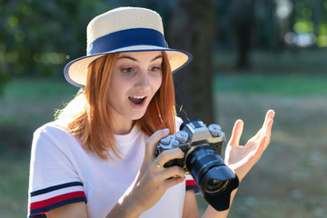 Pretty teenage girl with red hair looking amazed in photo camera in summer park.