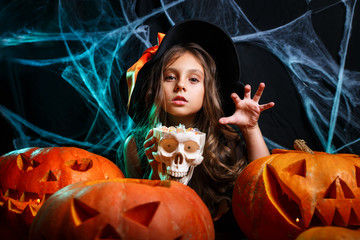 little witch child with halloween sweet and candy with cheerful smiling over spider web and with curved pumpkins
