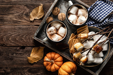 hot chocolate or cocoa drink and marshmallows in mugs and other sweets served on rustic wooden table