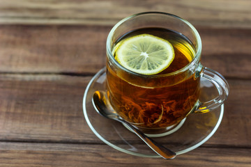 cup of hot tea with tea leaves and lemon on a wooden table
