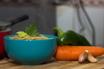 pasta servida en un bowl turquesa, acompañado de vegetales en una tabla de madera