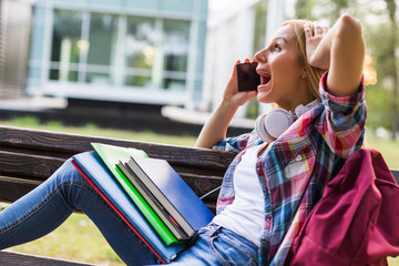 Fototapeta premium Female student in panic using phone while studying outdoor.