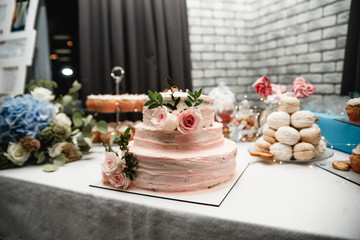 Wedding ceremony. Beautiful cake on the table. Elegant pink wedding cake decorated with roses with candy bar on background