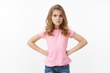 Offended cute sulking young blond little girl kid looking upset, frowning hold hands hips insulted, stare camera disappointed, waiting apologies, jealous brother ate her sweets, white background