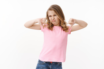Moody picky ignorant blond little girl kid, show thumbs down frowning, grimacing aversion and...