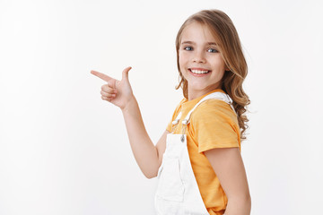 Curious clever pretty little girl found copy space, smiling amused and delighted, grinning playful,...