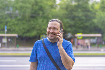 Adult man joyfully smiling speaks on the phone on a city street