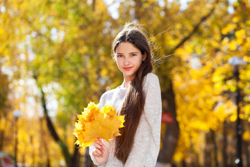 Portrait of a young beautiful girl with yellow maple leaves