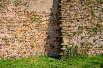 View of the stone fortress wall at the junction of the two parts. There is a step between the two parts of the wall. Between the stones on the wall, grass grows. Semur-en-Osua. Burgundy. France.