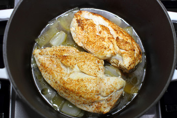 Delicious braised chicken breast cooked in a Dutch oven resting on the stove top in a home kitchen.