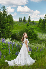 Romantic beautiful bride on sunny summer day outdoors. Young blonde woman in a beautiful wedding dress is posing in blooming field. Concept of wedding photoshoot in rustic style