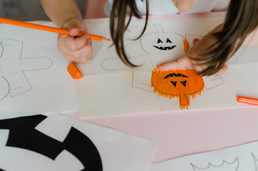 Mom with child makes Halloween decorations from paper. Child's and mother's hands and pumpkin, bats and other paper crafts for the holiday of Halloween.