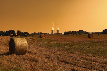  Thermal power plant with green field with hay bales. Sunset sky.