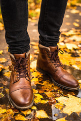 Man in brown leather boots standing in the puddle with autumn maple leaves. Conceptual trendy fall season image, hipster walking in the park