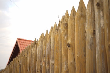 Fototapeta premium Fence made of sharp wooden stakes and red tiled roof under blue sky