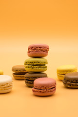 delicious various macarons stacked and some spread around on warm colored background 