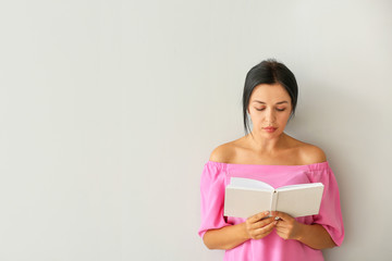 Portrait of beautiful woman reading book on light background