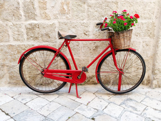 Fototapeta na wymiar Red bicycle with flower basket agains old stone wall on italian city street