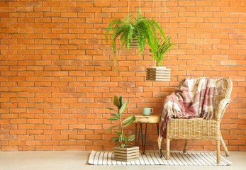 Wicker armchair, table and houseplants near brick wall