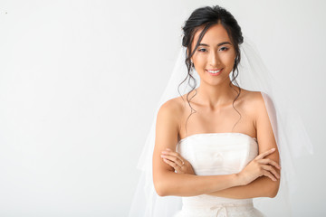 Beautiful young Asian bride on light background