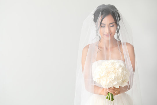 Beautiful young Asian bride on light background