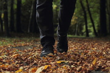 Closeup of man's legs in dark blue shoes walking in leaves on a pavement.