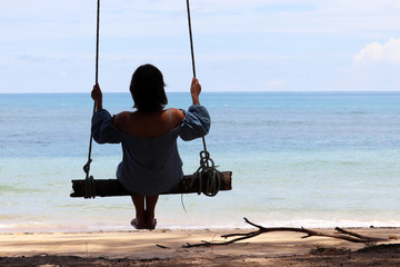 Silhouette of a girl swinging on a swing against the blue sea. Beach holidays, concept of freedom, happiness and romance