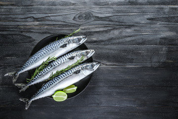 Plate with raw mackerel fish on dark table