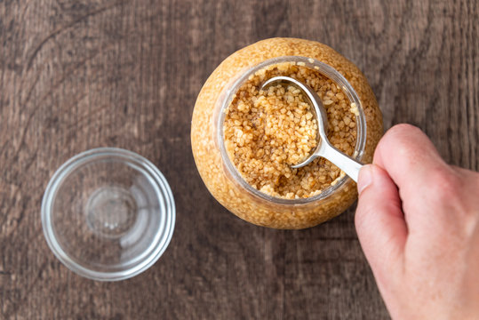 Glass jar of minced garlic and small glass bowl on wood background, woman&rsquo;s hand using tablespoon to scoop out garlic