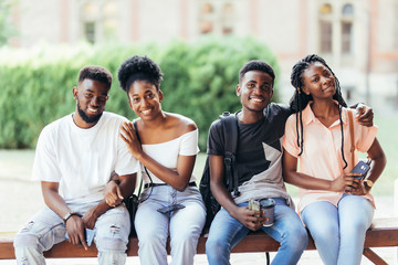 Group of young african friends students hanging out together outdoors on a bench and laughing as they discuss