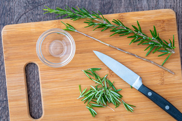 Fresh sprigs of rosemary with on a bamboo cutting board, with paring knife and small glass bowl