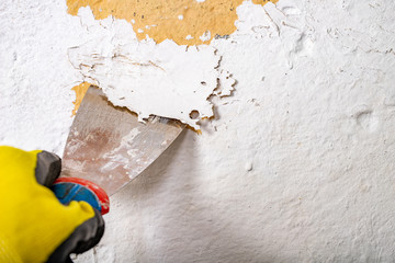 Removing old paint from the wall with a metal spatula. Small painting works at home. - obrazy, fototapety, plakaty