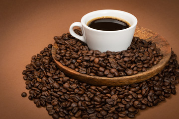 Hot coffee cup and coffee beans on brown background
