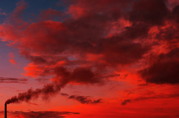 smoking chimney of a factory against fiery orange sunset. colorful and speckled  clouds.