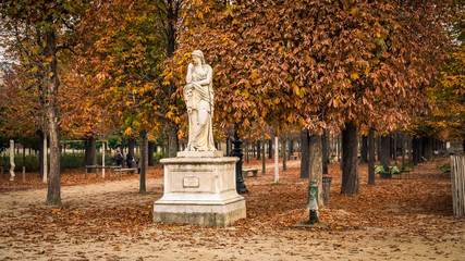 Alley of the Jardin des Tuileries covered with orange autumn leaves, statue in the Tuileries garden...
