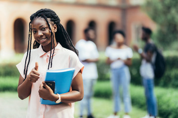 Portrait of happy young african woman with students in background on university campus