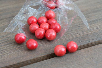 Red round candy spilled out of a transparent package and lie randomly on a wooden table. The table is made of rough boards. Selective focus.