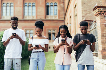 Happy group of friends students checking smart phones sitting at campus