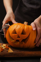 Hands cutting, carving pumpkin into jack-o-lanterns for halloween