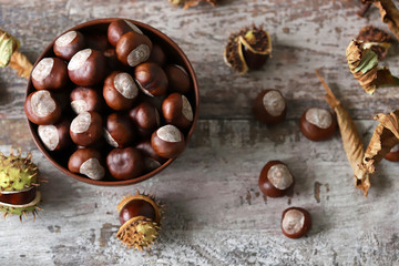 Chestnuts. A bowl of chestnuts. Leaves of a chestnut tree. Wood background. Selective focus.