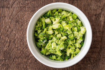 Round white bowl of chopped frozen broccoli on a dark wood background