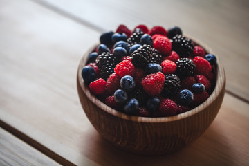 blueberries and raspberries, blackberry in a wooden bowl on old wood background