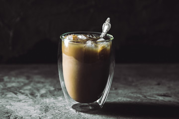 Pouring cream into a glass with iced coffee on table and black background