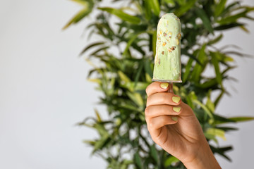 Female hand with tasty pistachio ice cream on blurred background