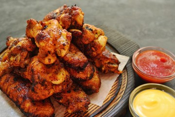 Fried chicken wings. Chicken wings on a dark background on a blackboard. Barbecue meat, grill. Sauce in bowls, ketchup, mayonnaise, mustard, cheese sauce. Appetizing fried meat. Place for your text