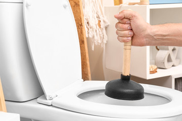 Man using plunger to unclog a toilet bowl
